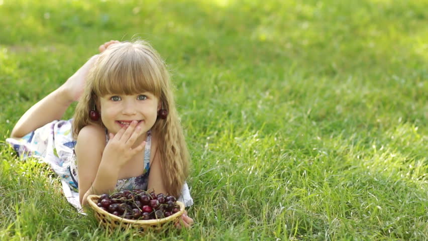 Child lying on the grass with a sweet cherry
