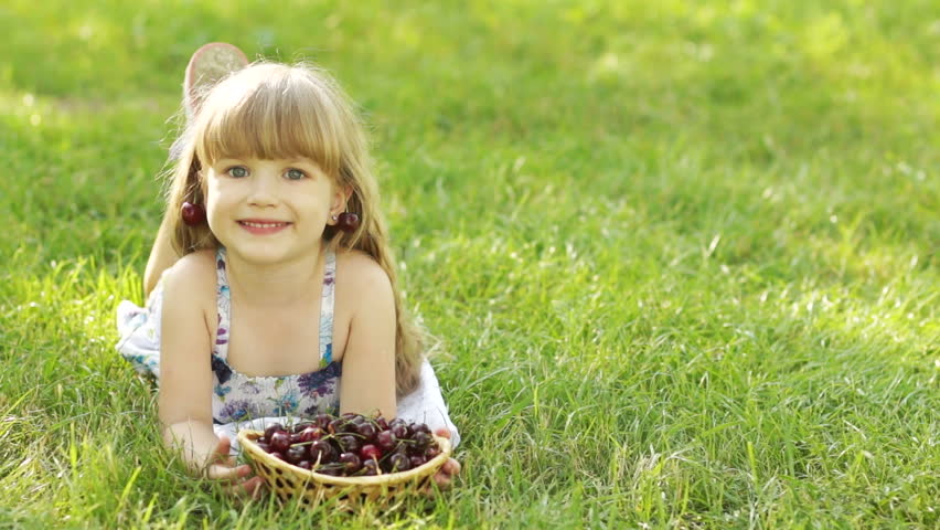 Child lying on the grass with a sweet cherry fruit
