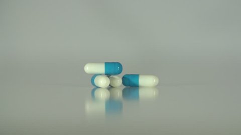 Extreme close up of pills & capsules falling in slow motion on a neutral background.