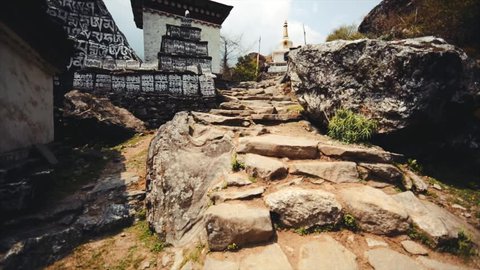 Ascending the cobblestone road in Nachipang village, the Himalaya, Nepal. View of nepali prayer stone and white stupa