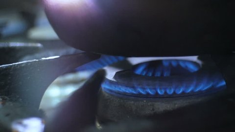macro gas flame flashes under large sauce-pan on gas stove burner in kitchen