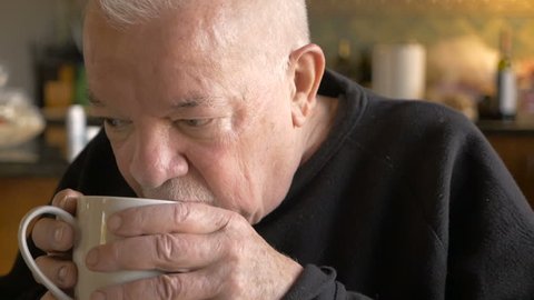 An attractive aging senior man drinking a cup of hot coffee or tea in slow motion