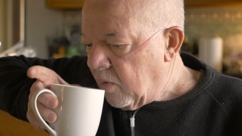 A senior man drinking coffee while wearing oxygen supplementation in slowmo