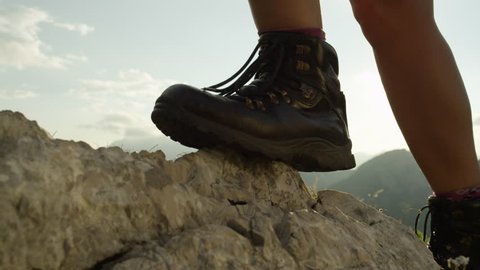 SLOW MOTION, CLOSE UP: Detail of vintage leather mountaineering boots. Unrecognizable adventurous female hiker climbing rocky mountains and walking uphill on amazing sunny summer day in European Alps