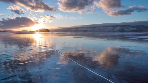 Drop a Piece of Ice on the Frozen Surface of Lake Baikal. 4K. Breaking the Ice on a Large Lake, winter break up on Lake Baikal. Blizzard on the ice. Siberian sunset.