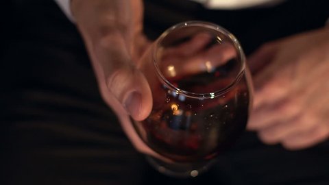 The glass with splashes cognac, slow motion. Glass of cognac in the man's hand.