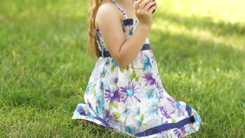 Girl sitting on the grass and eating a peach. Thumb up. Ok.
