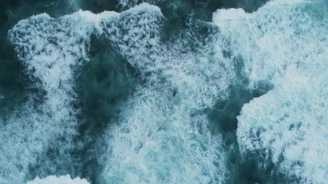 Aerial slow motion footage of waves. As the waves moves they create texture from white sea foam. The video is filmed from an overhead perspective. 