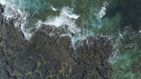 Slow motion shot of waves breaking on rocky shore at beach. Aerial drone footage of beautiful sea. The video is filmed from an overhead perspective.  