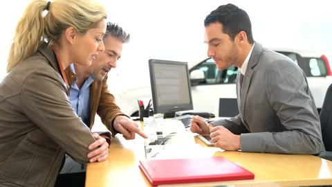 Salesman in car dealership and couple looking at catalogue