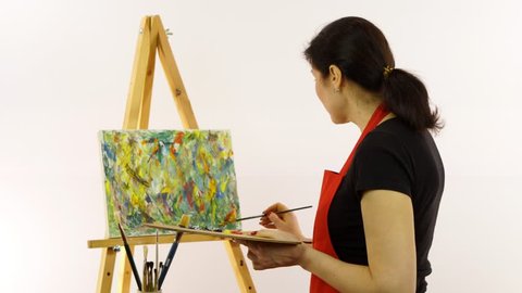 Woman artist painting with paintbrush. The woman draws a picture. The artist on a white background draws on an easel oil paints.  