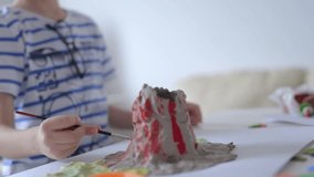 Boy painting clay in the shape of a volcano .Young little boy painting on the paper