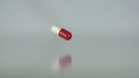 Extreme close up of a single tablet falling in slow motion. Medicine, drugs, pills, capsules falling in slow motion on a neutral background.