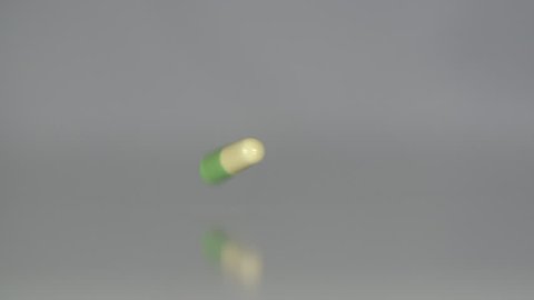 Extreme close up of a single tablet falling in slow motion. Medicine, drugs, pills, capsules falling in slow motion on a neutral background.