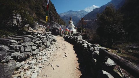 Walking along picturesque road in Benkar village, the Nepal Himalaya. View of nepali prayer stone and white stupa with colourful flags waving on wind