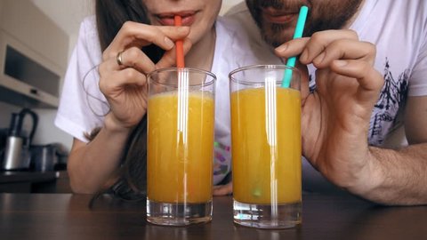 Young woman and man drinking orange juice with straws. Healthy lifestyle or funny competition concepts. 4K clip
