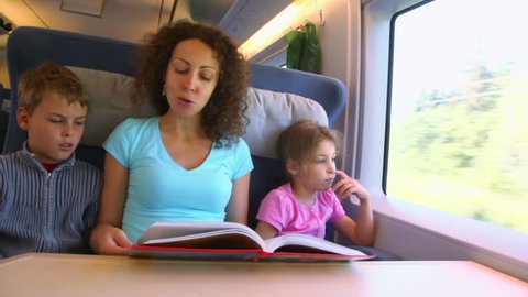 Mother reads book for two her children boy and girl when they travel in train