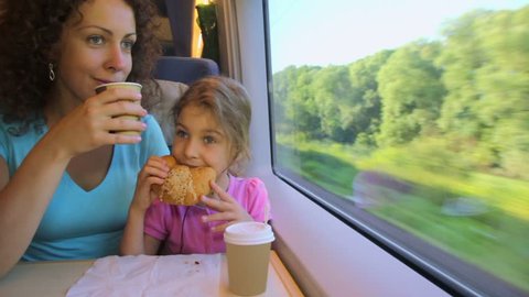 Mother drinks coffee and her little daughter eats marzipan when they travel in train near window