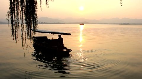 Silhouette of man rowing a small boat at sunset in West Lake, in the city of Hangzhou, China. Tourist attraction at twilight, travel destination concept