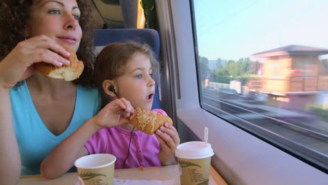Mother with her little daughter eat marzipans and watch to train window