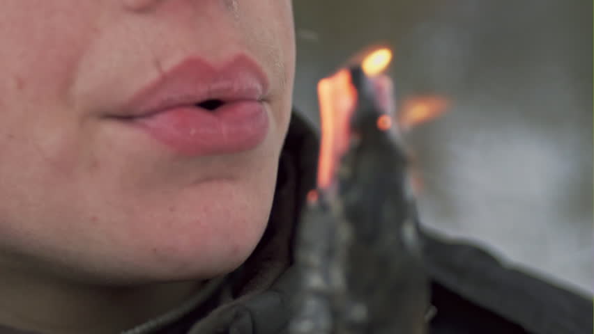 Young boy holding burning twig and fanning the fire on it. Slow motion.