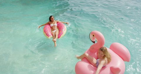 Two girls lying on inflatable flamingo Best friends having fun relaxing floating clear blue ocean Happy Women enjoying summer vacation tropical island beautiful beach bodies wearing bikini  TOP VIEW