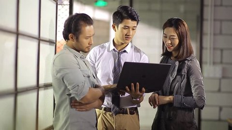 small group of young asian entrepreneurs discussing business using laptop computer in office. 