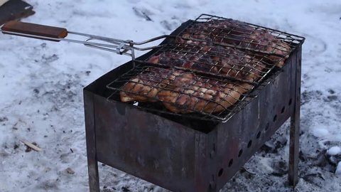 Man roasts barbecue on the grill in the winter and keeping the turns from one side of the handle to the other