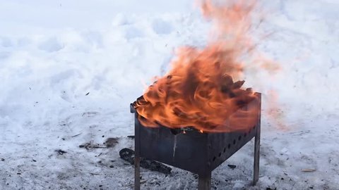 Burning wood in a brazier in the winter turned into charcoal for the barbecue. Bright fire on the snow