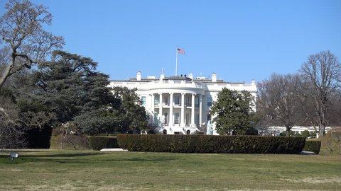 The White House in Washington DC with flag blowing in the wind. Snipers visible on the roof and fountain running.
