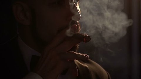 Silhouette of bearded Caucasian man who smoking a cigar, slow motion.