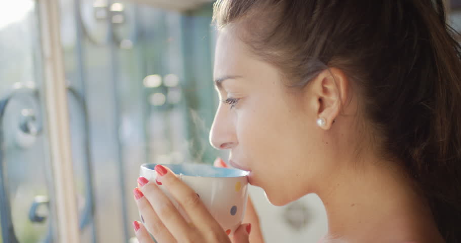 Beautiful young Woman drinking coffee alone at home looking out of window  | Shutterstock HD Video #24249980