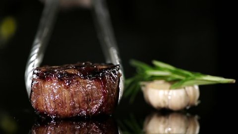 CLOSE UP FOOD: Cooking tongs put filet mignon on a black surface slow motion