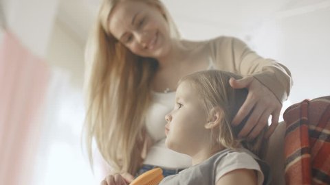 Sweet Young Mother Brushes Hair of Her Cute Little Blonde Daughter. Shot on RED EPIC-W 8K Helium Cinema Camera.