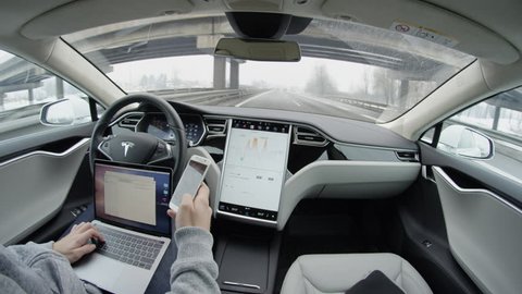 AUTONOMOUS TESLA CAR, FEBRUARY 2016: Business correspondence via smartphone and laptop from the car while traveling in self-driving autonomous automated driverless Tesla Model S electric vehicle