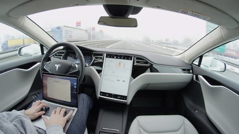AUTONOMOUS TESLA CAR, FEBRUARY 2016:  Luxury Tesla Model S autonomous automated electric car self-driving on highway on foggy winter morning. Young businessman working on notebook while traveling
