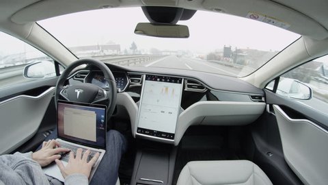 AUTONOMOUS TESLA CAR, FEBRUARY 2016:  Luxury Tesla Model S autonomous automated electric car self-driving on freeway in the morning. Unrecognizable businessman working on laptop while traveling