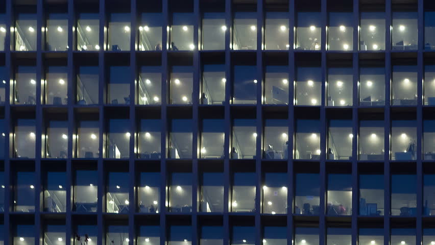 Office building, with illuminated interior at dusk, in the city of Barcelona. Panning Right and zoom out
