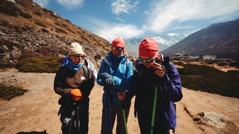 SHOMARE, NEPAL - APRIL 26, 2016: Three female trekkers watch into the camera, smile and wish other trekkers good fortune and health. Shomare-Dingboche path, Lhotse mnt (8516m) is on the background
