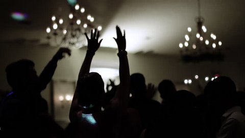 Group of silhouetted people dancing in a dark banquet hall for a wedding reception