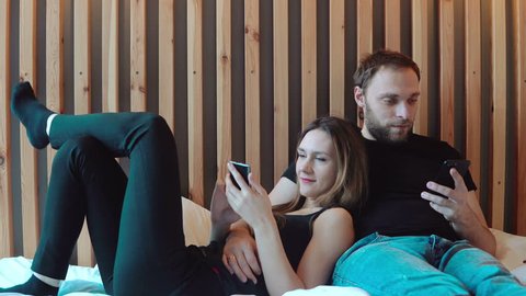 Young couple with smartphones lying on the floor. Man and woman use gadget to spend time, talk with each other.