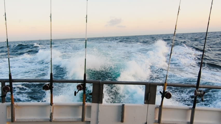 Powerful motors propel a fishing boat with fishing rods through the deep, blue waters of the ocean leaving a trail of white churned water in its wake. Royalty-Free Stock Footage #24294548