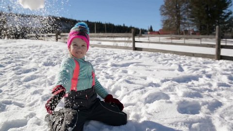 Playful Girl is Throwing Snowball at the Camera Enjoying Warm Winter Weather Outside. Female Child Having Fun Outdoors During Sunny Day.