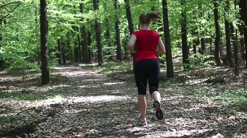 Young woman jogging in the forest, slow motion, dolly shot
