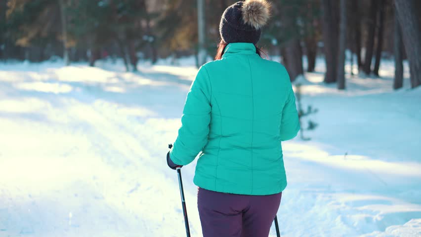 Woman nordic walking, enjoying the outdoors in winter park. Rear view. Long shot.