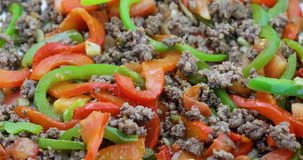 Close video of adding spaghetti sauce to browned ground beef, tomatoes, garlic, red and green bell peppers that are cooking.