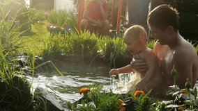 Cute little boy and his father, swimming, diving in a pool in the summer, having fun in slow motion happy grandma sitting on a swing on background beautiful flowers on foreground. 1920x1080