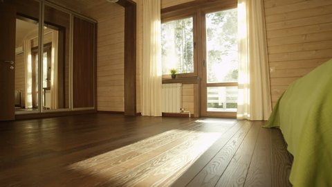 camera moves across bedroom through wide window to wooden sunlit terrace facing forest at sunset