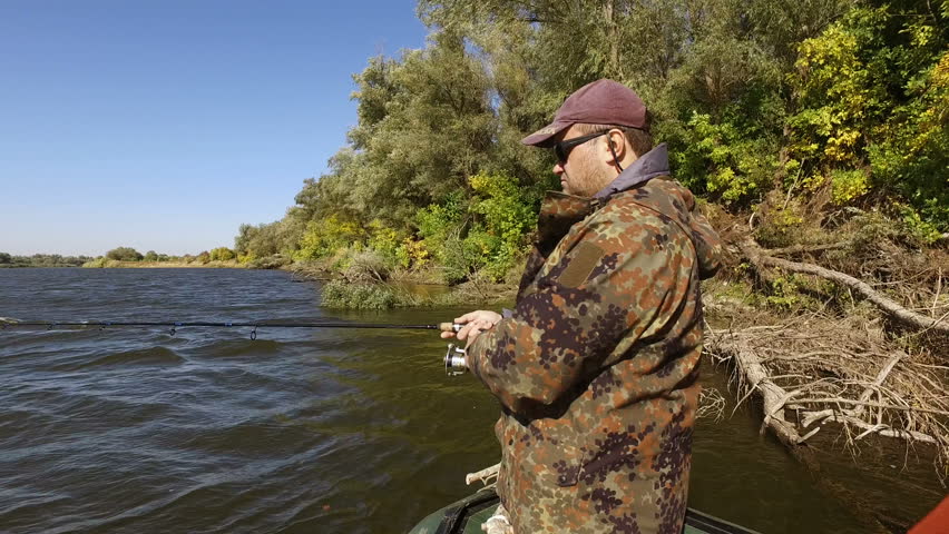 Scenic landscape. A young man is fishing while standing on a motor boat. 4K