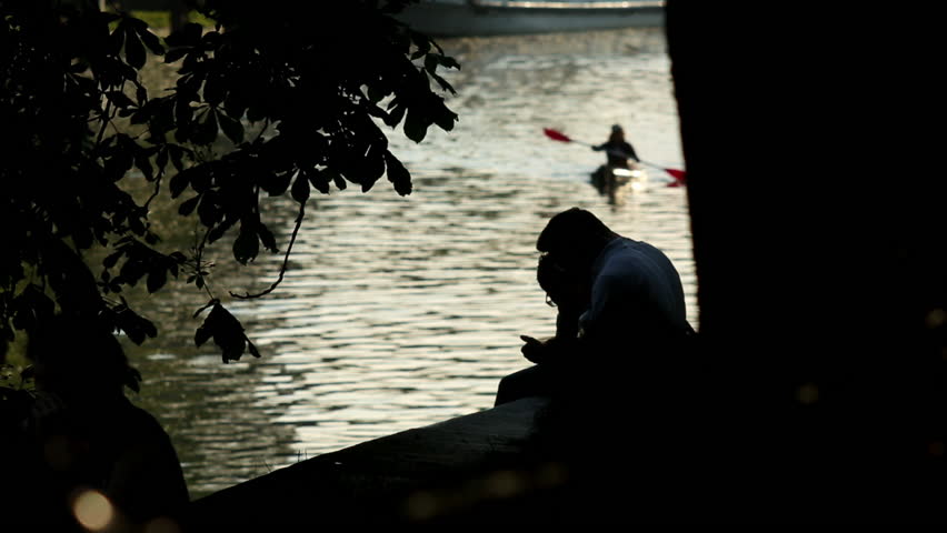 On the banks of the Spree in Berlin two men are chatting. They keep cell phones in their hands. On the river someone paddling past.
